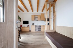 A room with a bed, wooden beams, a kitchen with cabinets, and a television.
