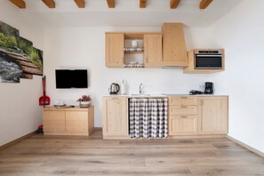 A modern kitchen with wooden cabinets, a built-in oven, a flat-screen TV, and a painting of a forest scene.