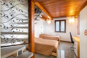 Une chambre avec deux lits, un bureau et un escalier orné de rampes en fer forgé.