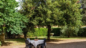 An outdoor table with chairs, surrounded by trees and a gravel path.