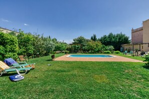 A backyard with a swimming pool, lawn chairs, and a pergola.