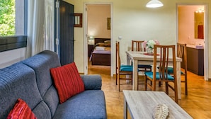 Una habitación con sofá, una mesa de comedor con sillas, una pequeña cocina y un baño visible a través de una puerta abierta.