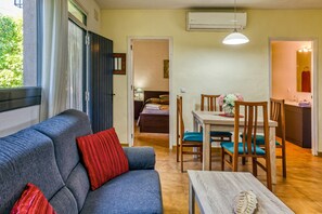 A room with a sofa, a dining table with chairs, a small kitchen area, and a bathroom visible through an open door.