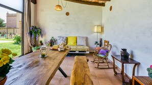 Una habitación acogedora con una mesa de madera, un banco, un sofá con cojines, una lámpara y una ventana con vistas a un jardín.