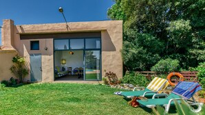 Una casa moderna con puerta de cristal que da a un patio, césped y mobiliario de exterior.