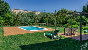 Un patio trasero con piscina, pérgola y mobiliario exterior.