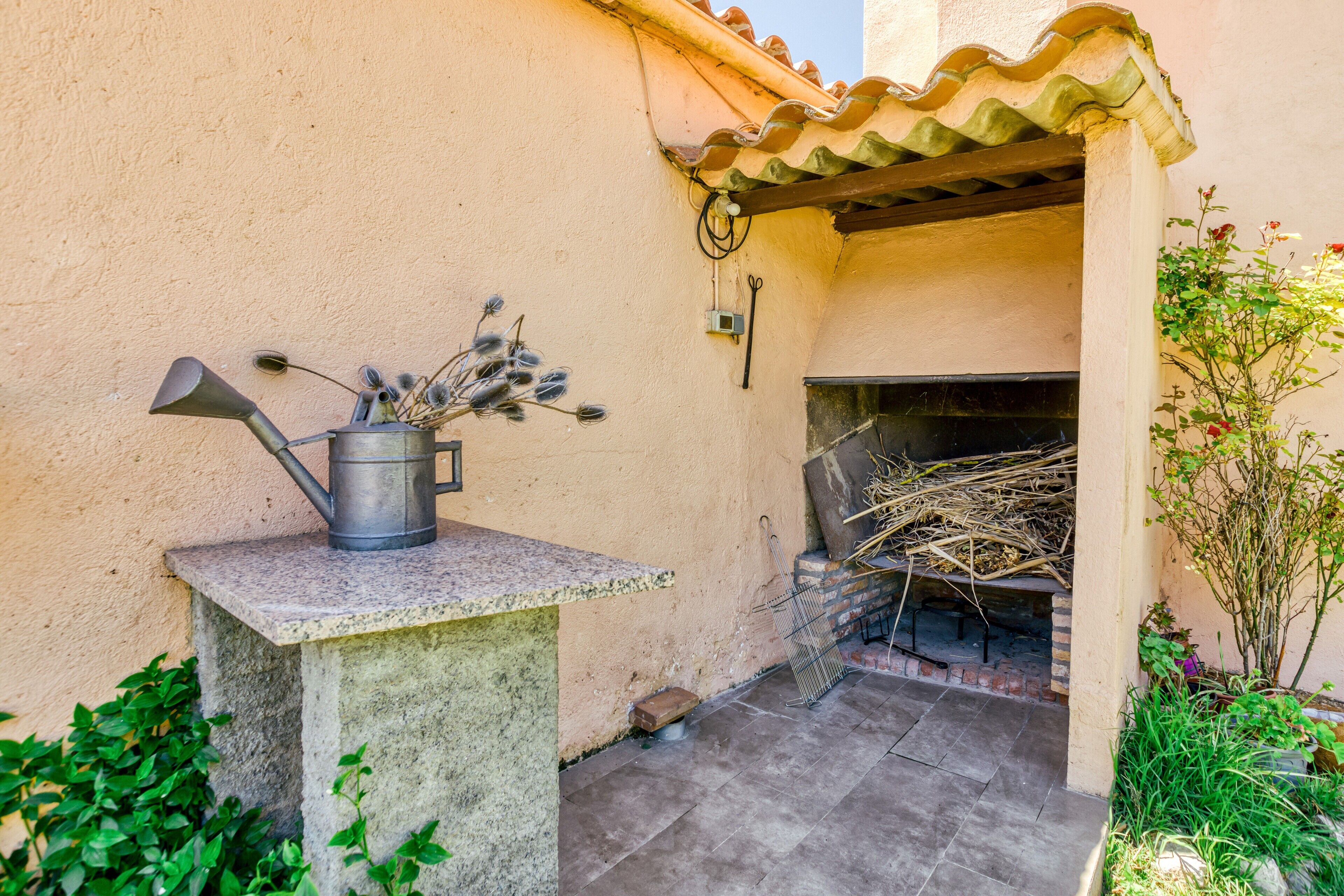 Un patio con un regadera de metal, una parrilla de ladrillo y una mesa de concreto.