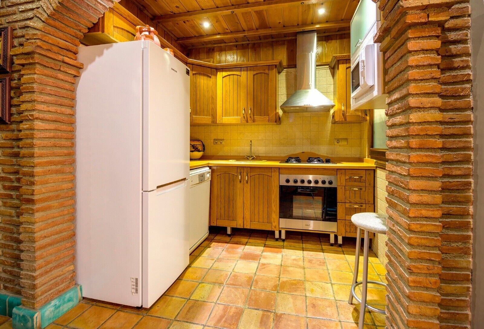 A kitchen with wooden cabinets, a white refrigerator, a stove, and a tiled floor.