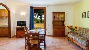Un coin repas comprenant une table et des chaises en bois, un téléviseur et un meuble avec des portes en verre.