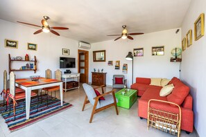A living room with a dining table, a sofa, a TV, and ceiling fans.