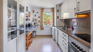 A compact kitchen with a washing machine, microwave, and a window with curtains.