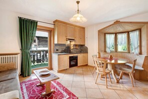 A cozy kitchen with wooden cabinets, a dining table with chairs, a built-in oven, and a view through a window with curtains.