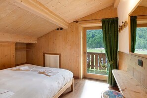Una habitación de madera con cama, ventana con cortinas, radiador y vista a un balcón.