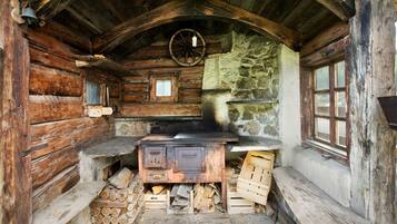 A rustic cabin interior with a wooden stove, stone wall, and a wooden bench.