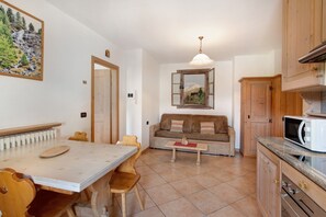 Un coin repas comprenant une table et des chaises, un canapé, une petite table basse, ainsi qu’une cuisine dotée de meubles en bois et d’un four à micro-ondes.