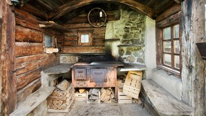 A rustic cabin interior with a wooden stove, stone wall, and a wooden bench. - Apartment "Larice Chalet Cambra" with Mountain View, Terrace & Garden (Livigno)