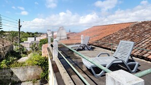 Una terraza en la azotea con dos sillones, una baranda metálica y vistas de un paisaje urbano con tejados de tejas rojas.