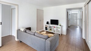 Una sala de estar moderna con un sofá gris, un televisor sobre un mueble blanco y piso de madera.