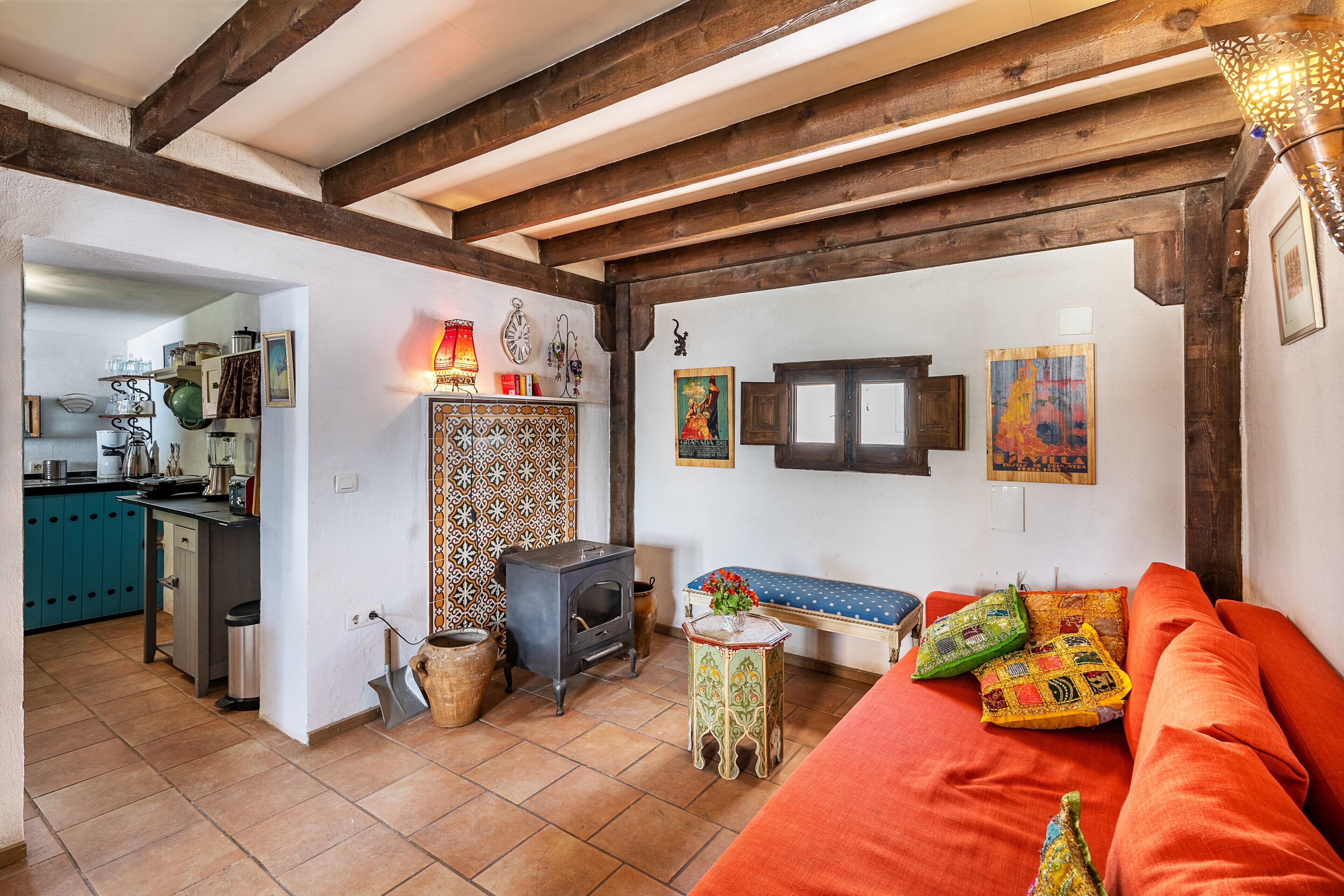 A cozy living room with a sofa, a small table, a decorative wall, and a kitchen area in the background.