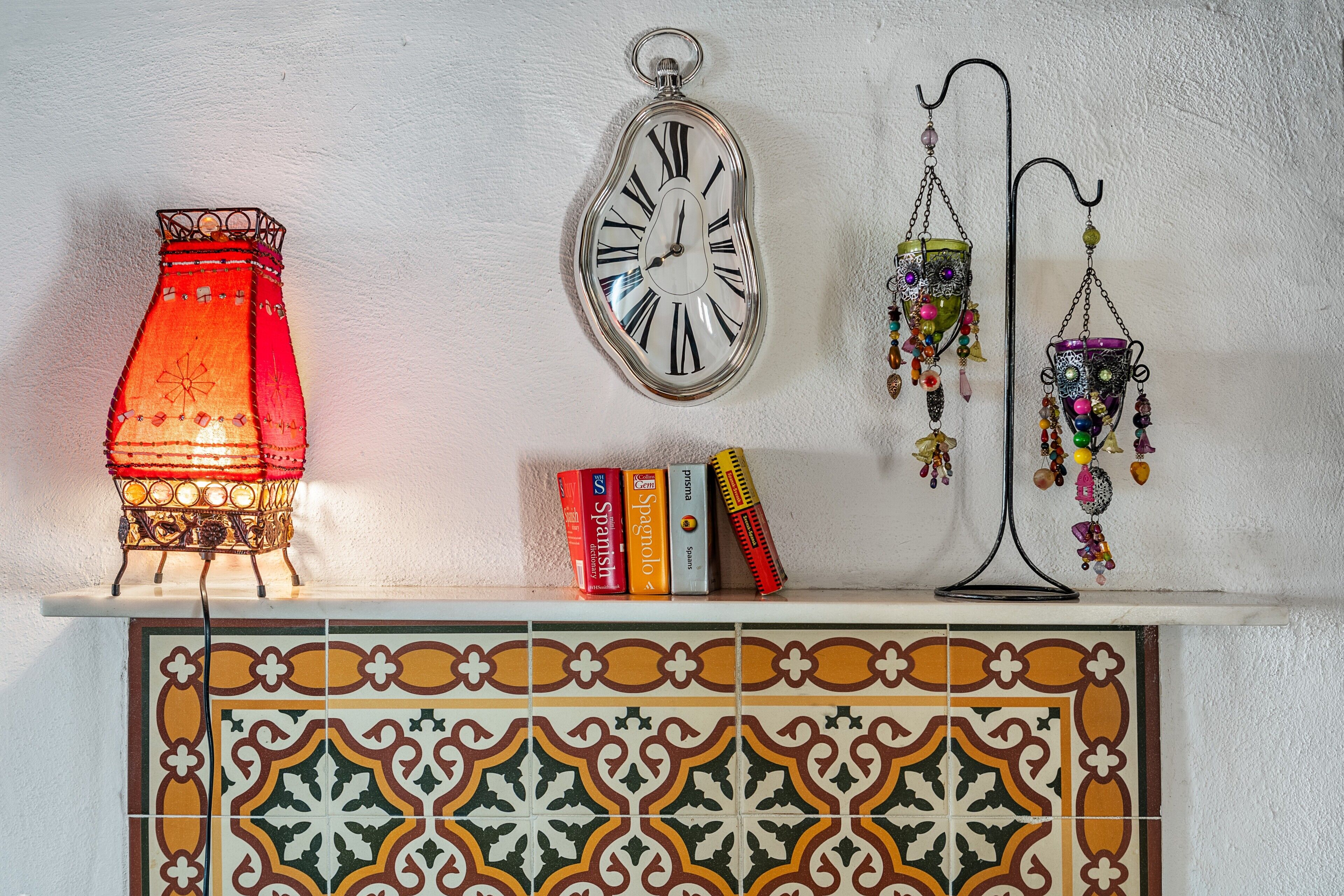 A shelf with a red candle holder, a wall clock, decorative hanging items, and books.