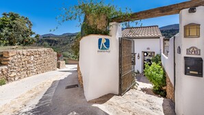 A rural villa entrance with a stone wall, a metal gate, and a clear view of the surrounding landscape.