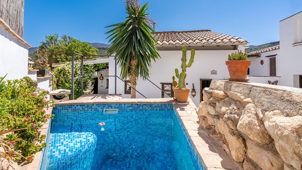 A swimming pool with clear blue water, surrounded by white buildings and a palm tree.
