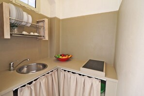 A kitchen with a sink, a dish rack, a bowl of fruit, and a window above the sink.
