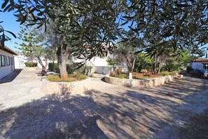 A residential area with a paved driveway, stone-bordered flower beds, and a white building with a red-tiled roof.
