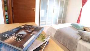 Una habitación con una cama, una mesa de madera con una revista, un armario y un ventanal corredero.
