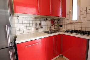 Une cuisine avec des meubles de couleur rouge, un réfrigérateur en acier inoxydable, une cuisinière à gaz et une fenêtre au-dessus de l’évier.