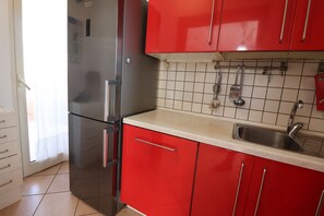 Una cocina con armarios rojos, un refrigerador de acero inoxidable, un lavamanos y un salpicadero de azulejos.