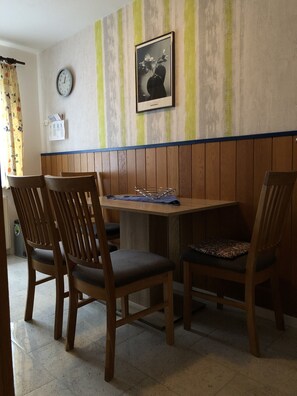 Un coin repas avec des chaises en bois et une table, une horloge au mur et un tableau encadré au-dessus de la table.
