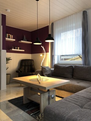 Una sala de estar moderna con una mesa de centro de madera, un sofá, una silla, luces colgantes y una estantería.