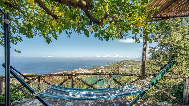 En hängmatta under en pergola med utsikt över havet och en kuststad.