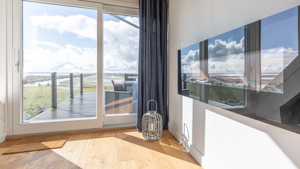A room with a large sliding glass door leading to a deck, a metal lantern, and a view of the beach. - Vacation home Arlau Schleuse in the Hattstedtermarsch for up to 4 people (Hattstedtermarsch)
