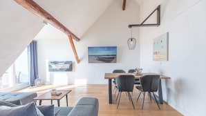 A modern living room with a wooden ceiling, a dining area with a wooden table and chairs, and a large window with curtains. - Vacation home Arlau Schleuse in the Hattstedtermarsch for up to 4 people (Hattstedtermarsch)
