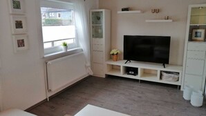 Un soggiorno moderno con una grande televisione a schermo piatto, mobili bianchi e una finestra con tende.