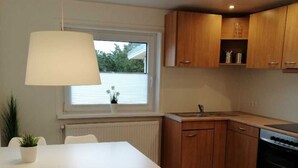 Una cucina moderna con mobili in legno, un piano di lavoro bianco e un forno integrato. C'è un tavolo da pranzo con sedie e una lampada a sospensione sopra.