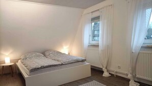 Una camera da letto con un letto, un comodino, una finestra con tende e un termosifone.