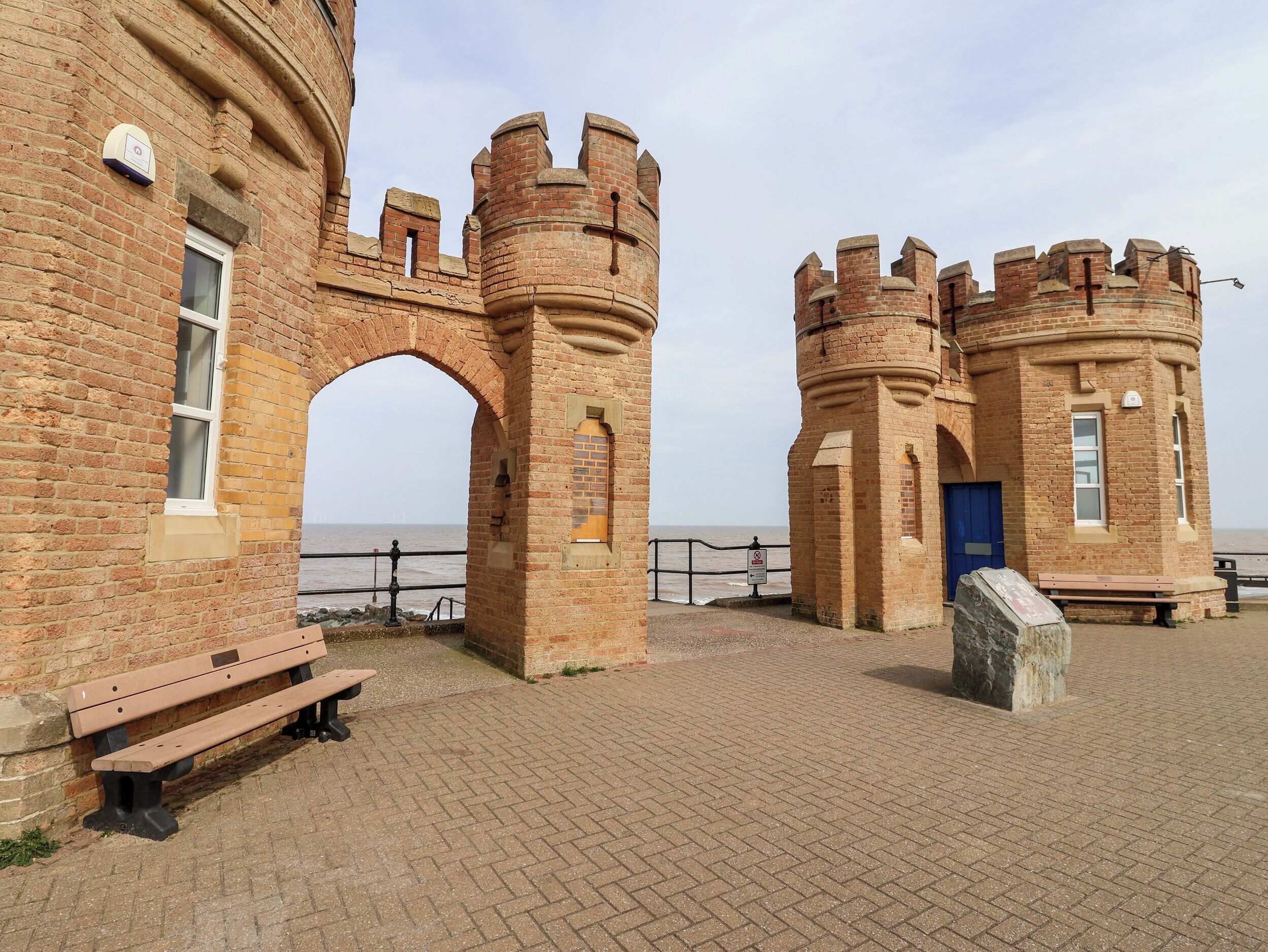 A historic brick building with arched gateways and a bench.
