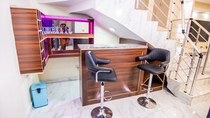 Zona de bar moderna con dos taburetes negros, una barra de madera y un espejo con iluminación rosa.
