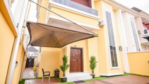 Un edificio amarillo con puerta marrón, un balcón y dos macetas con plantas.