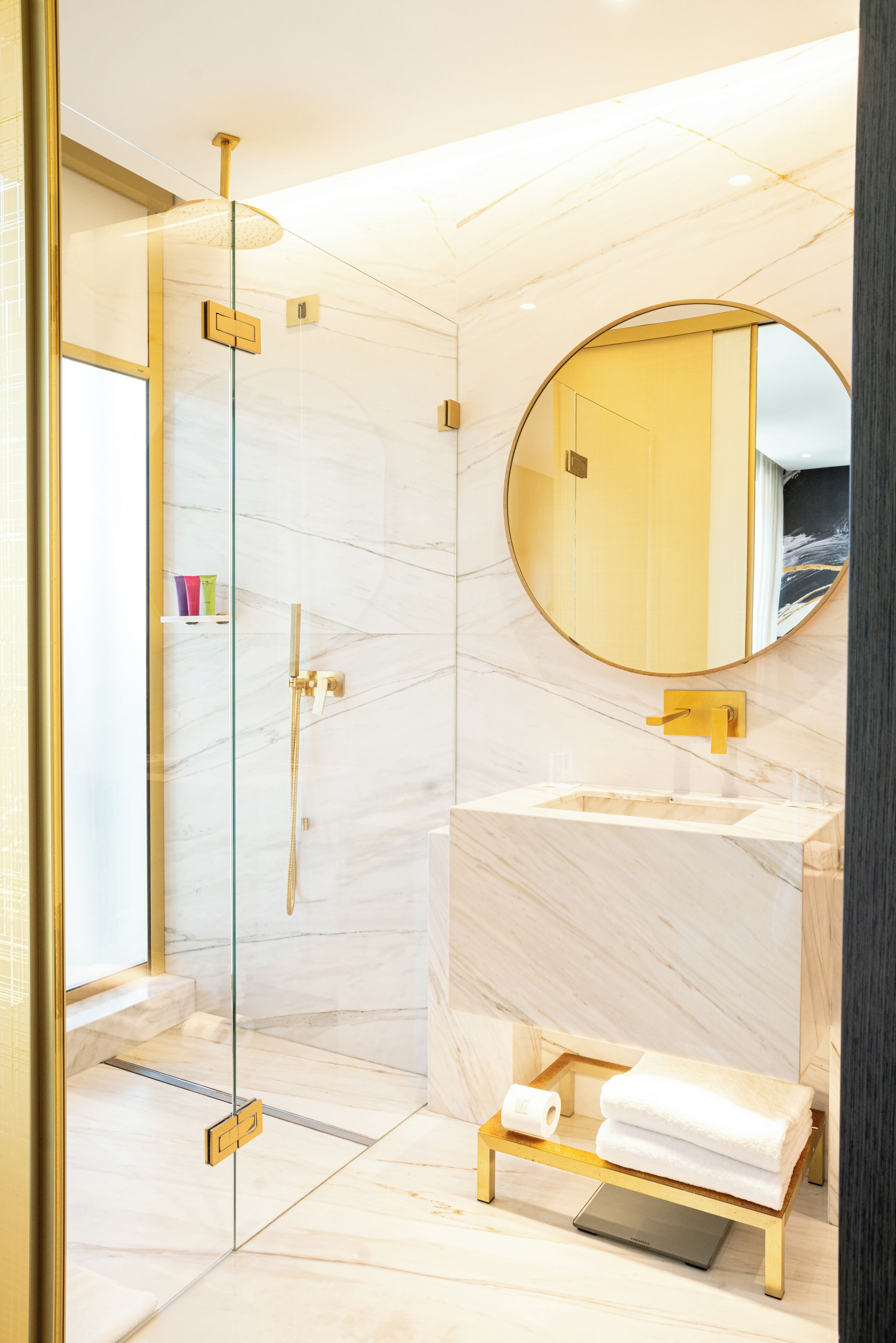 Un baño moderno con ducha de vidrio, tocador de mármol y espejo redondo.
