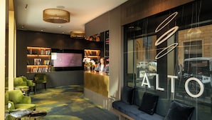 A modern lobby with a reception desk, seating area, and a large window with the word "ALTO" on it. - The First Musica - Preferred Hotels & Resorts (Rome)