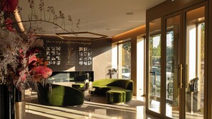 A modern interior with a green sofa set, a glass door leading outside, and a wall with framed photos. - The First Musica - Preferred Hotels & Resorts (Rome)