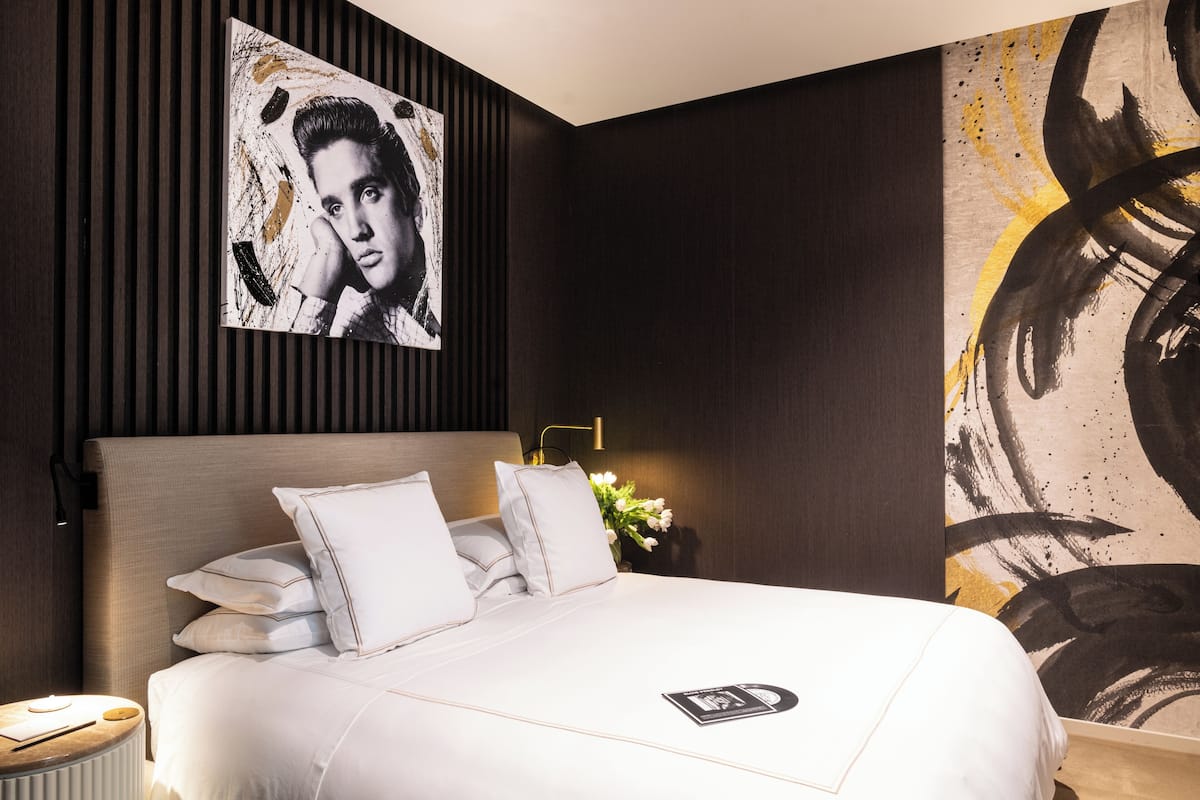 A modern hotel room with a large bed, a nightstand, a lamp, and artwork on the walls.