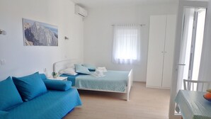 Une chambre à coucher avec un lit, un canapé, une petite table et une fenêtre avec des rideaux.