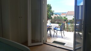 Une pièce dotée d’une porte-fenêtre coulissante donnant sur une terrasse extérieure avec une table et des chaises.