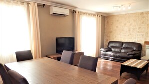 A dining area with a wooden table and chairs, a television, and a leather sofa.