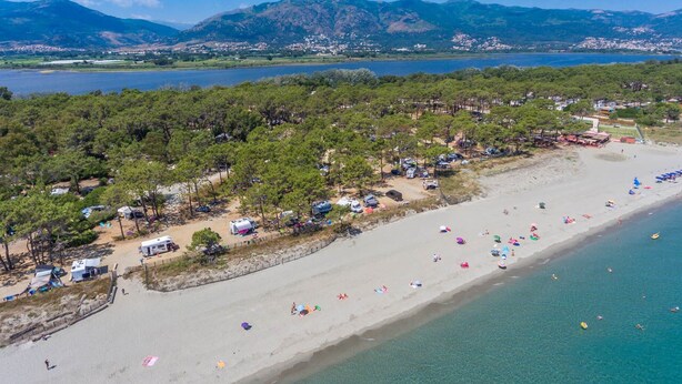 A beach with tents and RVs, a sandy shore, and a lake in the background.